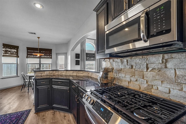 kitchen with light wood-style flooring, stainless steel appliances, a peninsula, visible vents, and backsplash