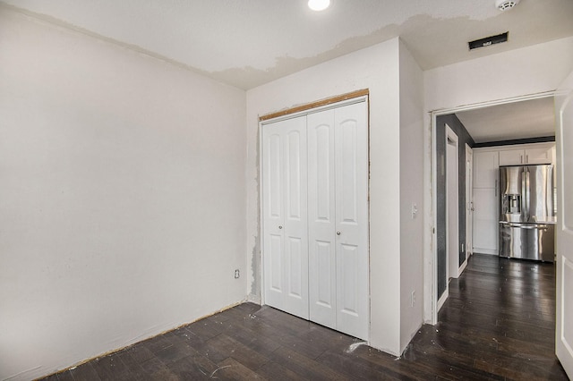 unfurnished bedroom with dark wood-type flooring, a closet, and stainless steel fridge