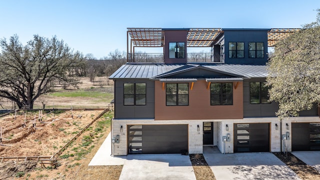 contemporary home with a garage, a standing seam roof, driveway, and a balcony