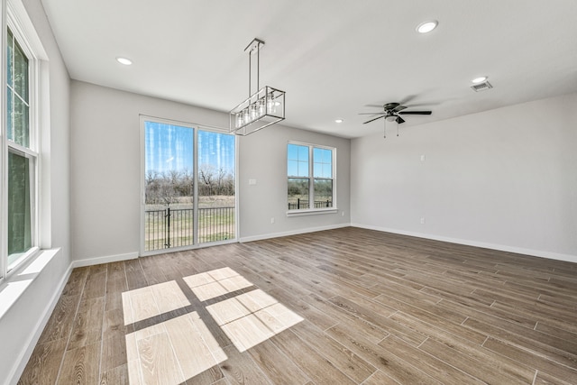 unfurnished dining area featuring recessed lighting, visible vents, wood finished floors, baseboards, and ceiling fan with notable chandelier