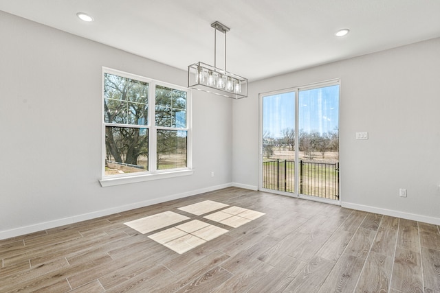 unfurnished dining area with a notable chandelier, recessed lighting, wood finished floors, and baseboards