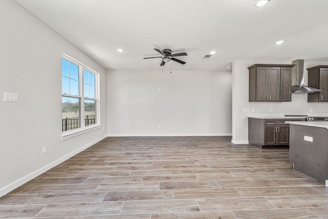 kitchen featuring open floor plan, dark brown cabinets, light countertops, wood tiled floor, and wall chimney exhaust hood