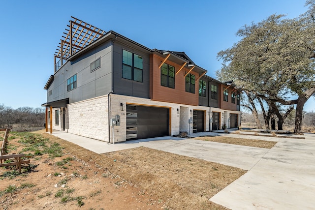 contemporary house featuring concrete driveway, stone siding, and an attached garage