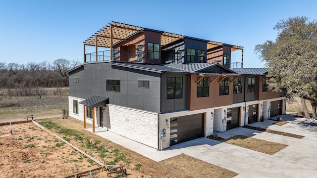 view of front of house with metal roof, an attached garage, a balcony, concrete driveway, and a standing seam roof