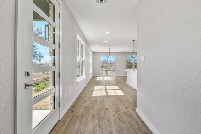 hall featuring baseboards, an inviting chandelier, visible vents, and light wood-style floors