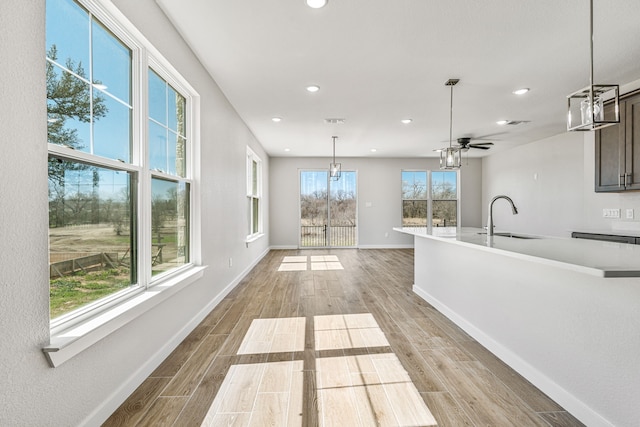 kitchen featuring decorative light fixtures, light countertops, light wood-style flooring, a sink, and baseboards