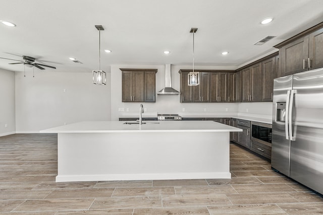 kitchen with dark brown cabinetry, wall chimney exhaust hood, stainless steel appliances, wood finish floors, and a sink