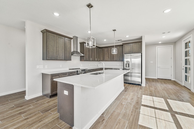 kitchen with dark brown cabinetry, wall chimney range hood, stainless steel appliances, and a sink