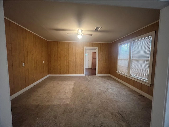 spare room with carpet, crown molding, visible vents, wooden walls, and baseboards