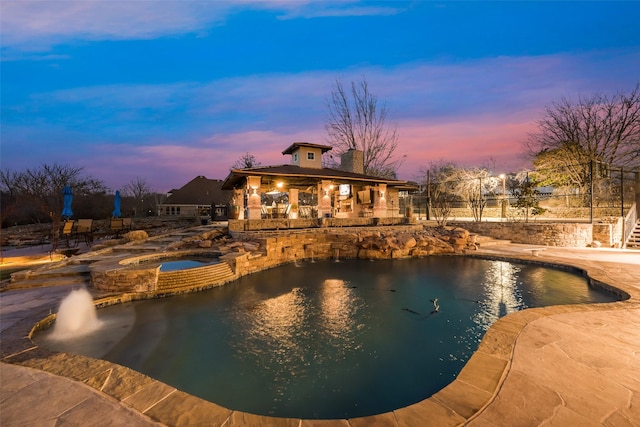 pool at dusk featuring a patio area, an outdoor pool, and an in ground hot tub