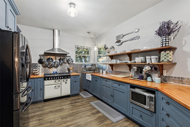 kitchen featuring stainless steel appliances, butcher block countertops, open shelves, a sink, and wall chimney exhaust hood