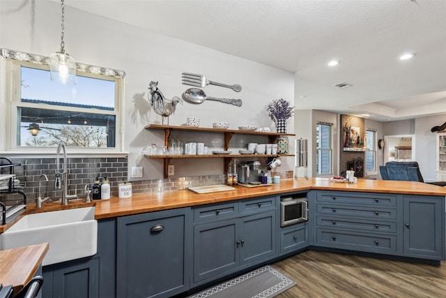 kitchen with dark wood-style floors, pendant lighting, a sink, wooden counters, and backsplash