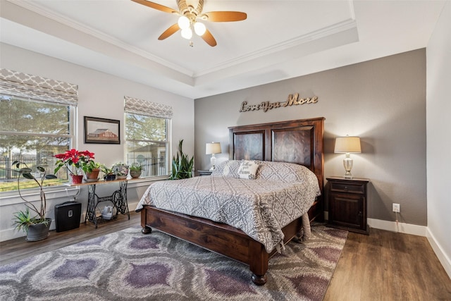 bedroom featuring ornamental molding, a tray ceiling, wood finished floors, and baseboards