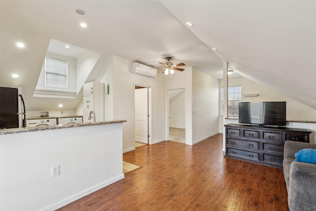 interior space featuring lofted ceiling, a wall unit AC, freestanding refrigerator, light stone countertops, and hardwood / wood-style floors