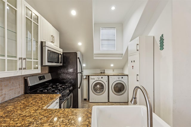 kitchen featuring stainless steel appliances, a sink, white cabinets, independent washer and dryer, and tasteful backsplash