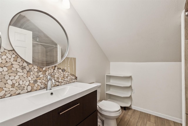 bathroom featuring toilet, wood finished floors, vanity, vaulted ceiling, and decorative backsplash