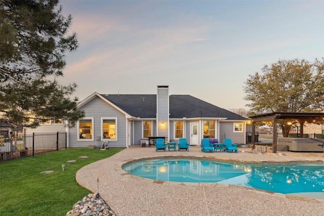 pool at dusk featuring a yard, fence, a hot tub, and a patio