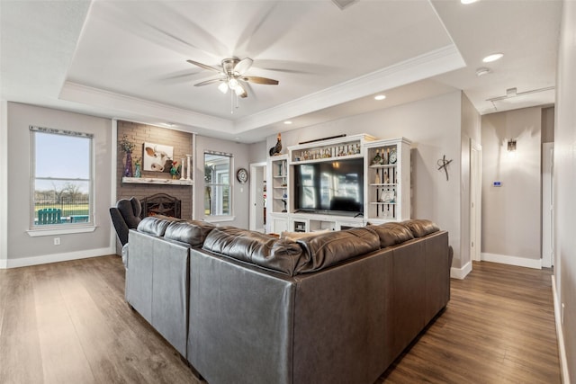 living room with a brick fireplace, plenty of natural light, a tray ceiling, and wood finished floors