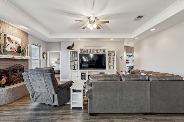 living area featuring a brick fireplace, visible vents, crown molding, and dark wood-style flooring