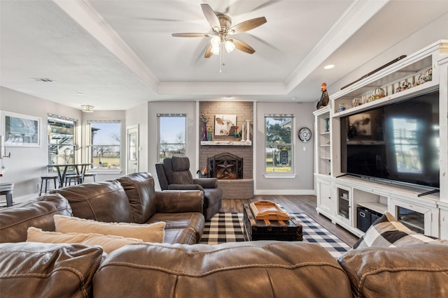 living room with a raised ceiling, visible vents, ornamental molding, a brick fireplace, and wood finished floors