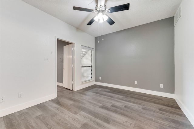 unfurnished room with ceiling fan, wood finished floors, visible vents, and baseboards