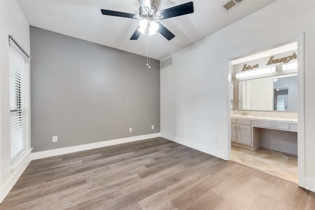 unfurnished bedroom featuring ensuite bath, light wood-style flooring, visible vents, and a sink