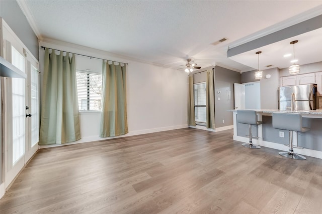 unfurnished living room featuring light wood-style floors, a textured ceiling, visible vents, and crown molding