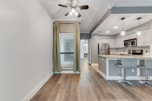 kitchen with appliances with stainless steel finishes, a kitchen bar, white cabinets, and crown molding