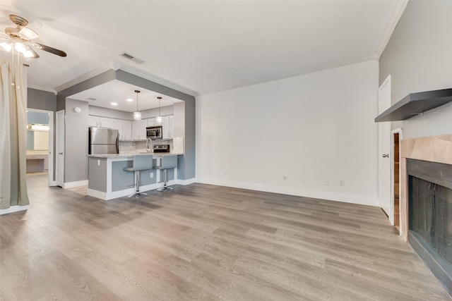 unfurnished living room featuring visible vents, a tiled fireplace, ornamental molding, light wood-type flooring, and baseboards