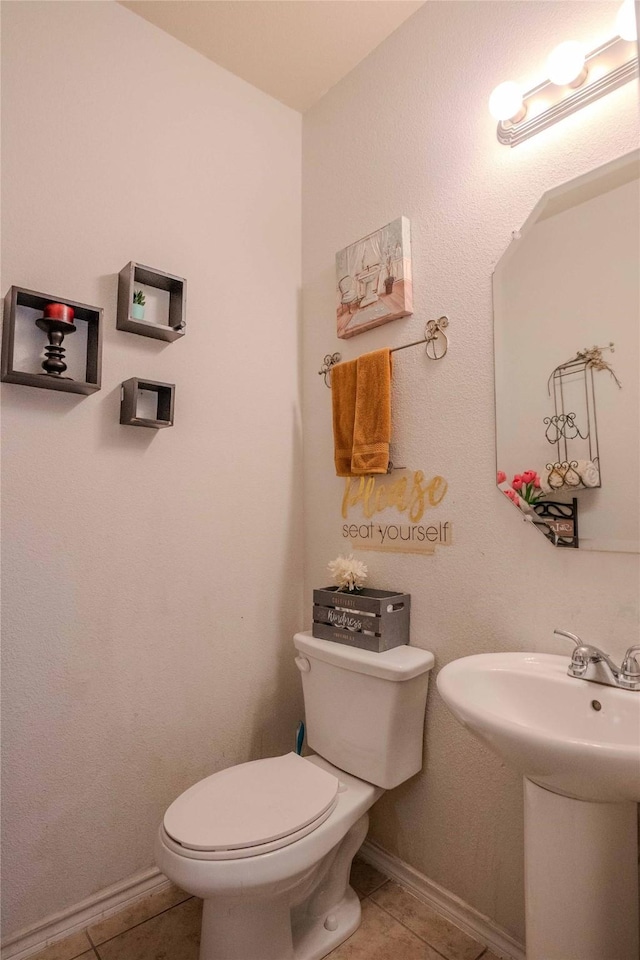 half bathroom with a sink, tile patterned flooring, toilet, and baseboards