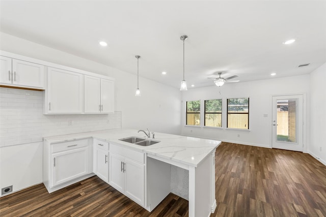 kitchen featuring a peninsula, a sink, white cabinets, and light stone countertops