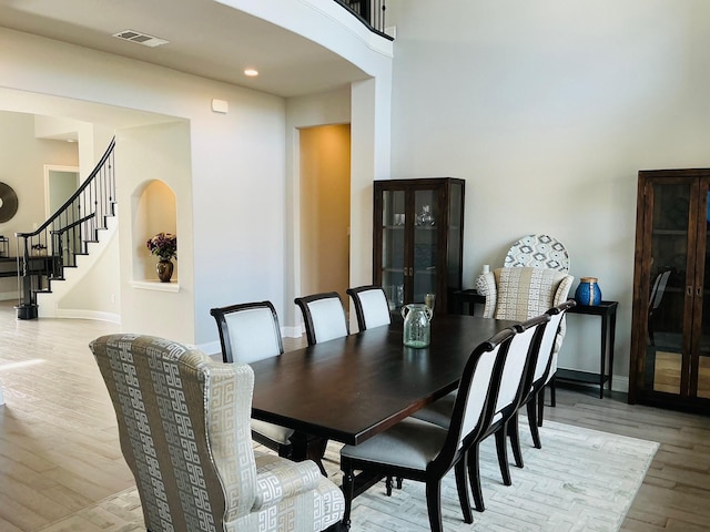 dining space featuring arched walkways, light wood finished floors, visible vents, stairway, and baseboards