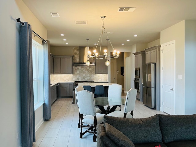 kitchen featuring visible vents, appliances with stainless steel finishes, an inviting chandelier, gray cabinets, and wall chimney range hood