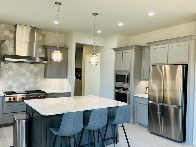 kitchen featuring light stone counters, gray cabinetry, a kitchen island, appliances with stainless steel finishes, and wall chimney exhaust hood