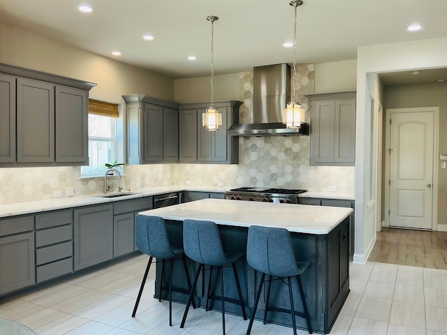 kitchen featuring gray cabinetry, a kitchen island, a sink, a kitchen breakfast bar, and wall chimney range hood