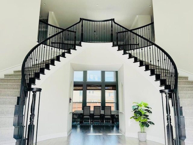 staircase featuring a towering ceiling, baseboards, and wood finished floors