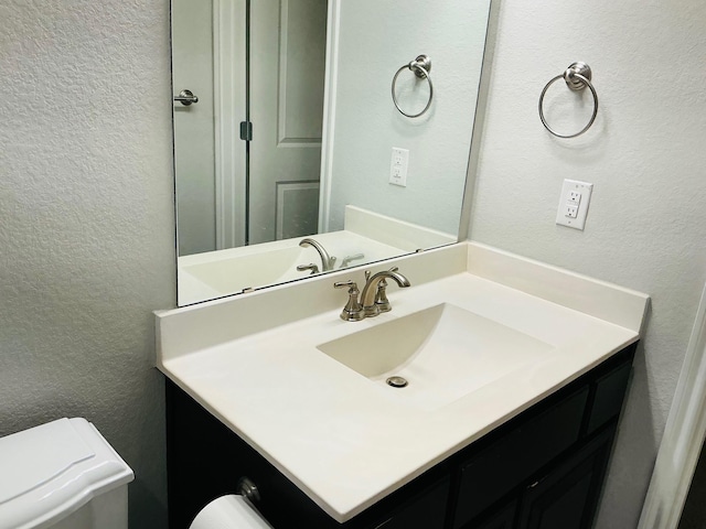 half bath featuring a textured wall, vanity, and toilet