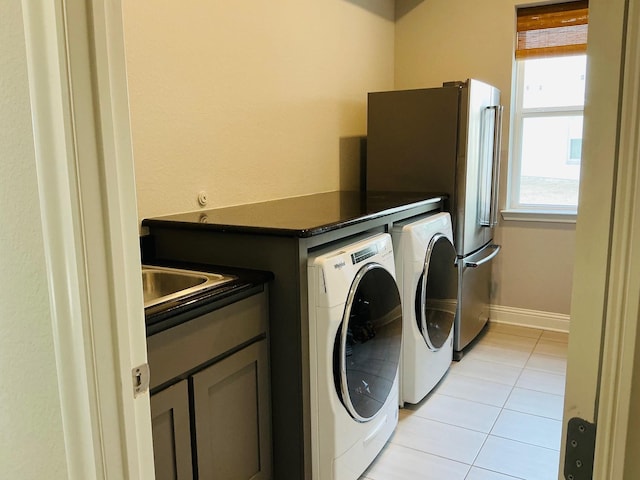 clothes washing area with light tile patterned floors, cabinet space, baseboards, separate washer and dryer, and a sink