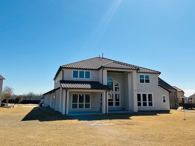 back of house with a lawn, a tiled roof, and stucco siding