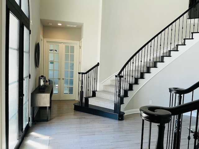 entrance foyer with a high ceiling, wood finished floors, french doors, stairway, and plenty of natural light