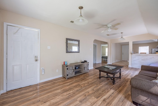 living area with baseboards, visible vents, a ceiling fan, wood finished floors, and vaulted ceiling