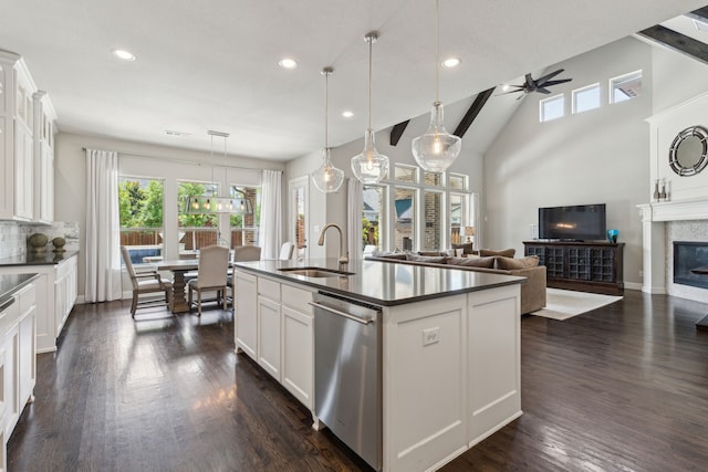 kitchen with a sink, stainless steel dishwasher, dark wood-style floors, dark countertops, and a glass covered fireplace