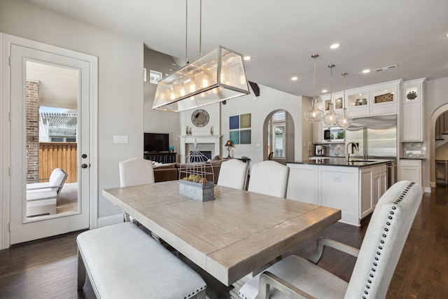 dining area with arched walkways, recessed lighting, a fireplace, visible vents, and dark wood-style floors