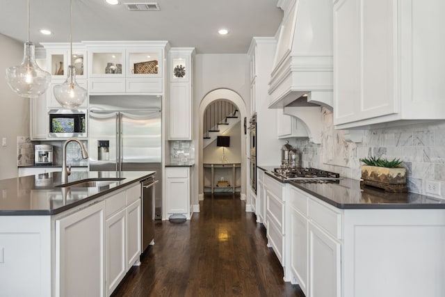 kitchen featuring dark countertops, a sink, white cabinetry, and custom range hood