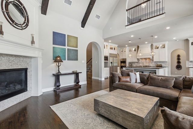 living room with a glass covered fireplace, beam ceiling, visible vents, and dark wood finished floors