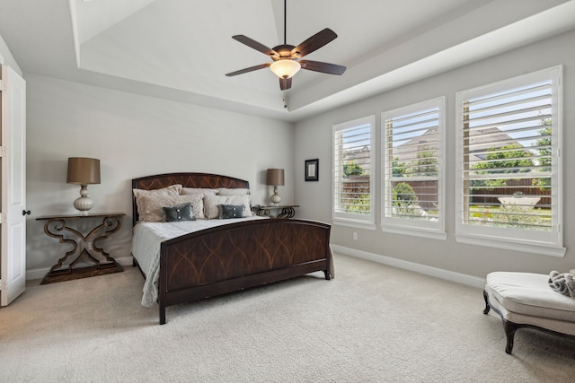 carpeted bedroom featuring baseboards, a raised ceiling, and a ceiling fan