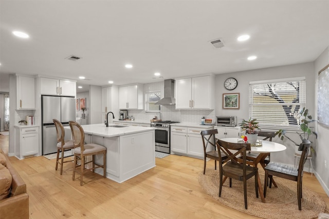 kitchen featuring visible vents, wall chimney exhaust hood, appliances with stainless steel finishes, light wood-style floors, and a sink