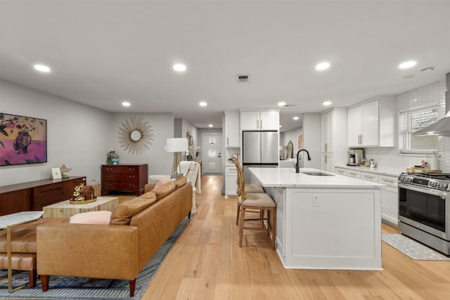 kitchen with appliances with stainless steel finishes, a breakfast bar, open floor plan, light wood-type flooring, and a sink