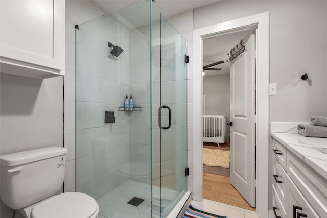 full bath featuring toilet, wood finished floors, vanity, a stall shower, and radiator heating unit