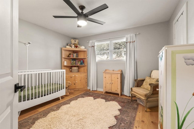 bedroom featuring a ceiling fan, a nursery area, and wood finished floors